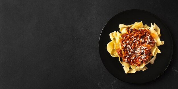 Makaron pappardelle z sosem ragout wołowym w czarnej misce na szarym tle kopia przestrzeń