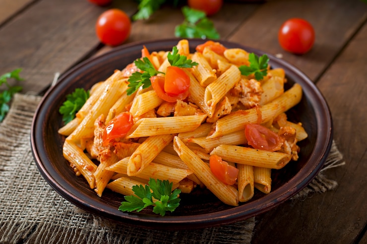 Zdjęcie makaron penne w sosie pomidorowym z kurczakiem i pomidorami na drewnianym stole