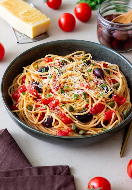 Makaron spaghetti Alla Puttanesca z kaparami Kalamata oliwki ser pomidory i anchois włoskie jedzenie