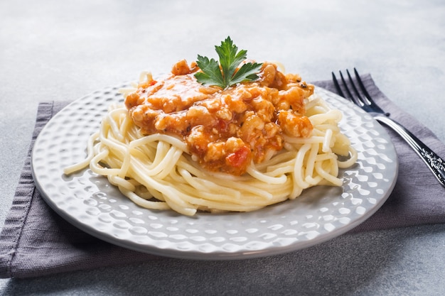 Makaron spaghetti Bolognese na białej płytce, szary stół