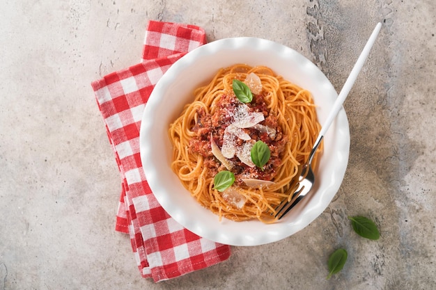 Makaron spaghetti Bolognese Smaczne apetyczne włoskie spaghetti z sosem bolońskim sos pomidorowy ser parmezan i bazylia na białym talerzu na szarym tle kamiennego lub betonowego stołu Widok z góry