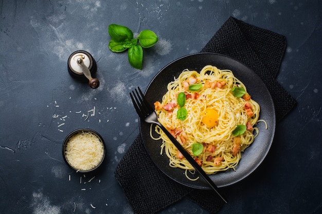 Makaron Spaghetti Carbonara Z Boczkiem, Parmezanem, żółtkiem I Listkami Bazylii Na Czarnej Powierzchni. Tradycyjne Włoskie Danie