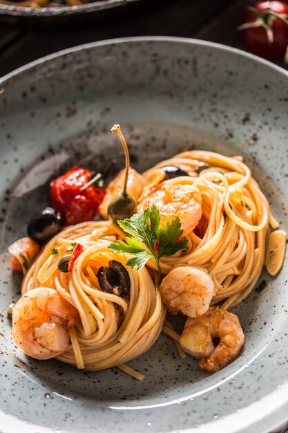 Makaron spaghetti na talerzu i patelni z krewetkami w sosie pomidorowym z pomidorami i ziołami. Kuchnia włoska lub śródziemnomorska.
