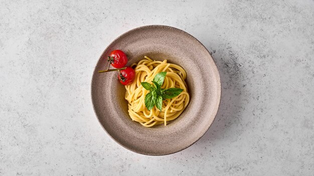 Makaron spaghetti z pieczonymi pomidorami cherry i bazylią na talerzu ceramicznym na jasnym tle płaski lay