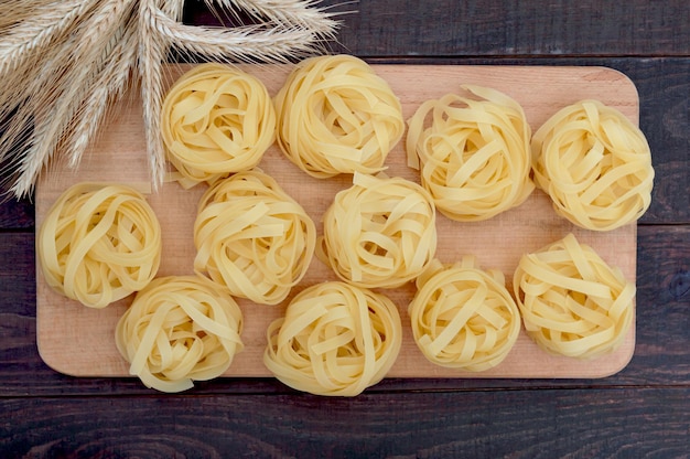 Makaron Tagliatelle W Formie Gniazd Na Desce Do Krojenia Z Kłoskami Pszenicy. Widok Z Góry.