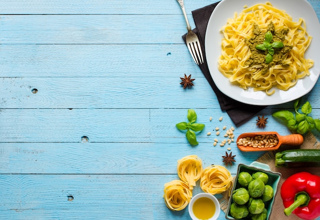 Makaron tagliatelle z sosem pesto i innymi warzywami na drewnianym tle. Widok z góry