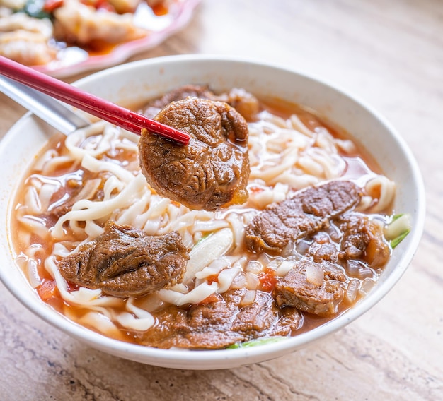 Makaron wołowy Tajwan ramen posiłek z bulionem z sosem pomidorowym w misce na jasnym drewnianym stole słynne chińskie jedzenie z bliska widok z góry kopia przestrzeń