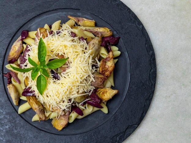 Makaron z czarnymi oliwkami, parmezanem, sercami karczochów, posypany świeżą bazylią.