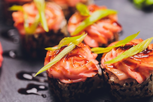 Maki Sushi Rolls z łososiem na czarnym kamieniu na ciemnym tle. Z imbirem i wasabi. Menu sushi. Japońskie jedzenie. Zbliżenie na pyszne japońskie jedzenie z rolką sushi. Poziome zdjęcie.