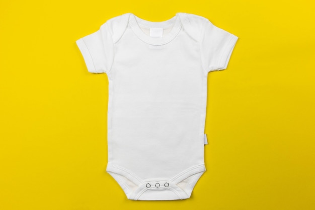 Makieta białego body niemowlęcego płasko leżała na żółtej powierzchni