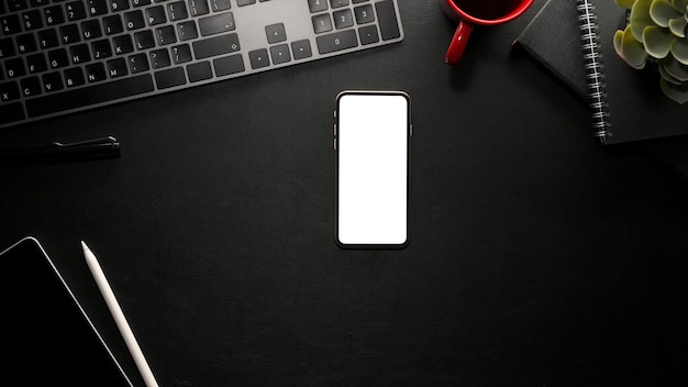 Makieta białego ekranu smartfona na nowoczesnym czarnym stole biurowym z akcesoriami. widok z góry