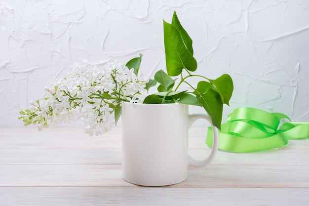 Makieta białego kubka do kawy z białą liliową i zieloną wstążką. Pusty kubek makiety do promocji projektu, stylizowany szablon