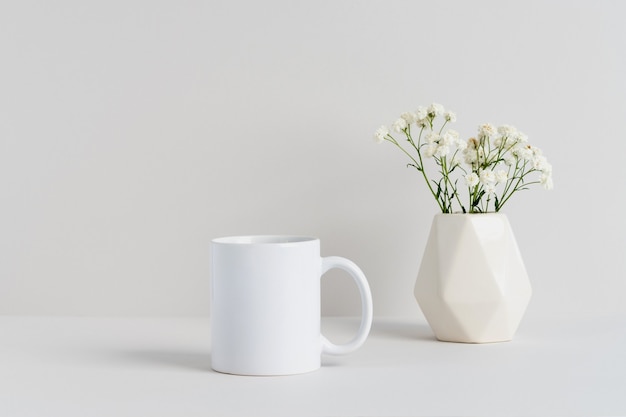 Zdjęcie makieta białego kubka z beżowym wazonem i gałązką gipsówki na stole