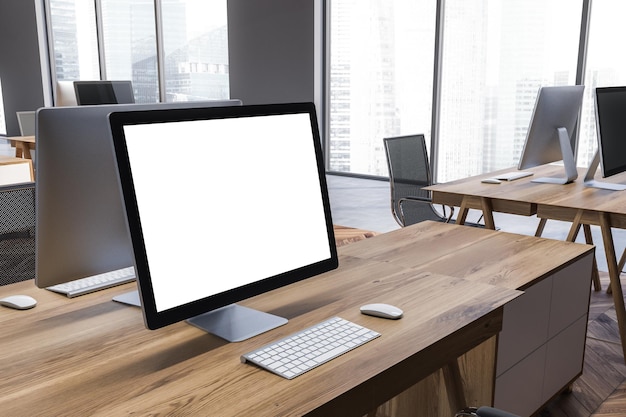 Makieta ekranu komputera stojącego na drewnianym stole w nowoczesnym biurze z szarymi ścianami, drewnianą i betonową podłogą oraz panoramicznymi oknami. renderowania 3D