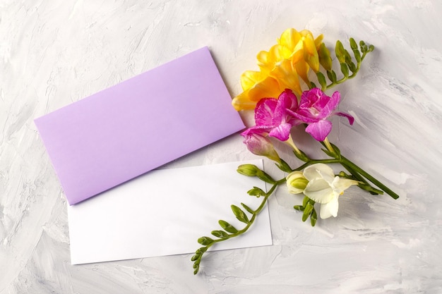 Makieta kartki z życzeniami z kolorowymi kwiatami frezji i kopertą z życzeniami na betonowym tle