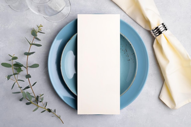 Makieta karty menu na niebieskim talerzu ze świątecznym ustawieniem stołu weselnego lub urodzinowego z gałązką eukaliptusa na szarym tle