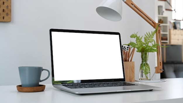 Makieta laptopa z pustym ekranem filiżanka kawy i uchwyt na ołówki na białym stole w domowym biurze