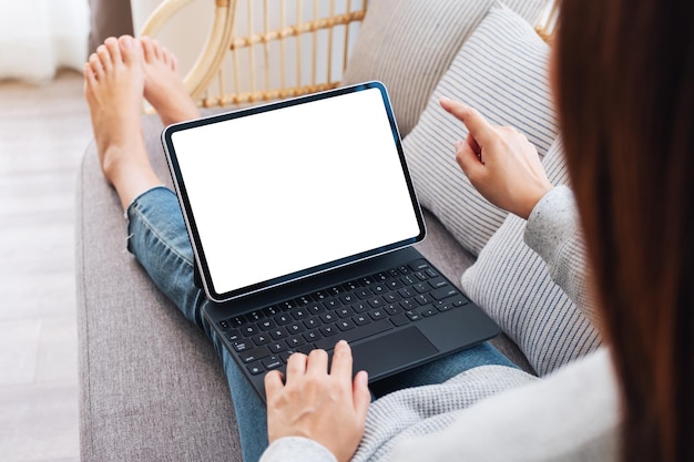 Makieta obrazu kobiety korzystającej z czarnego komputera typu tablet z pustym białym ekranem pulpitu jako komputera PC, leżąc na kanapie w domu