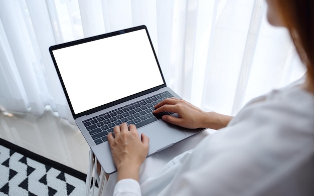 Makieta obrazu kobiety pracującej i piszącej na komputerze przenośnym z pustym ekranem siedząc w sypialni w domu