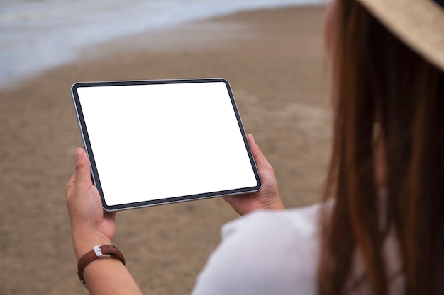 Makieta obrazu kobiety trzymającej czarny komputer typu tablet z pustym ekranem pulpitu nad morzem