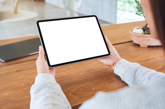 Makieta obrazu kobiety trzymającej czarny tablet pc z pustym białym ekranem na drewnianym stole