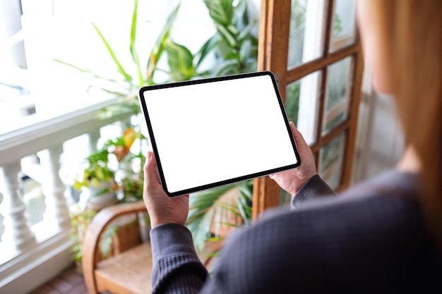 Makieta obrazu kobiety trzymającej i używającej cyfrowego tabletu z pustym białym ekranem pulpitu na balkonie w domu