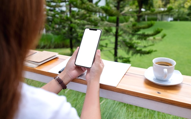 Makieta obrazu kobiety trzymającej telefon komórkowy i używającego go z pustym białym ekranem pulpitu na zewnątrz