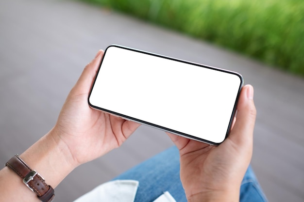 Makieta obrazu kobiety trzymającej telefon komórkowy z pustym białym ekranem pulpitu na zewnątrz