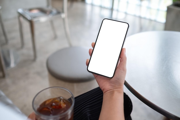 Makieta obrazu kobiety trzymającej telefon komórkowy z pustym białym ekranem pulpitu podczas picia kawy