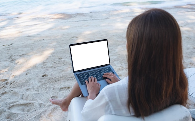 Makieta obrazu kobiety używającej i piszącej na komputerze przenośnym z pustym ekranem pulpitu podczas siedzenia na plaży