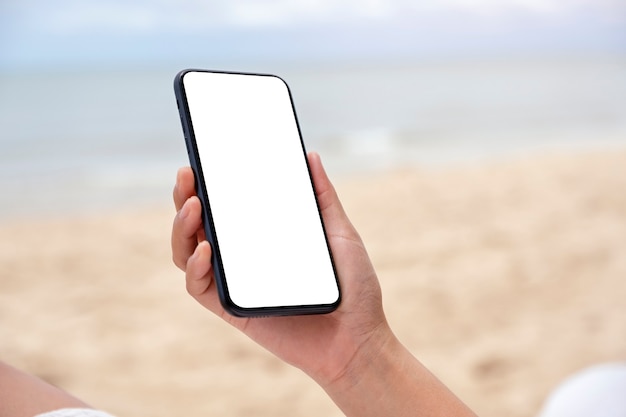 Makieta obrazu rąk trzymających czarny telefon komórkowy z pustym ekranem pulpitu nad morzem