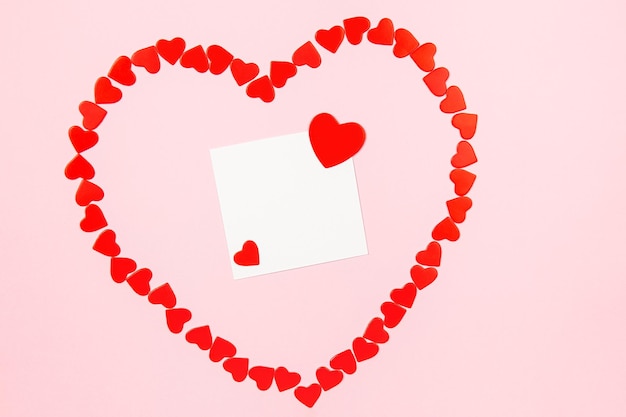 Zdjęcie makieta papierowej kartki z życzeniami lub karty życzeń na różowym tle wzór wiecznego pióra czerwonych serc do pisania pozdrowień i życzeń widok z góry
