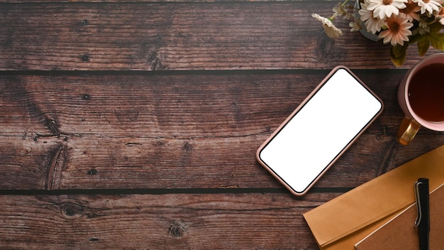 Makieta smartfona z filiżanką kawy z białym ekranem i kwiatami na drewnianym biurku