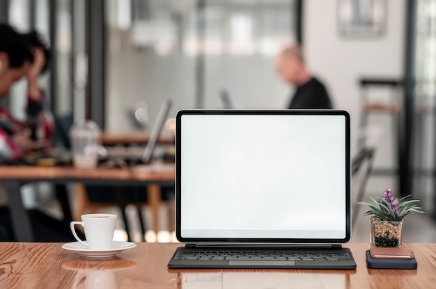 Makieta tablet z pustym ekranem z klawiaturą na drewnianym stole w kawiarni.