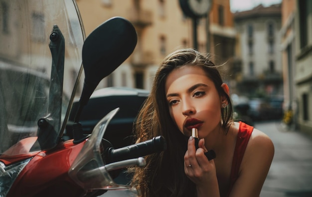 Zdjęcie makijaż w ruchu moda dziewczyna z czerwonymi ustami umieścić szminkę patrząc w lustro motocyklowej ulicy fa