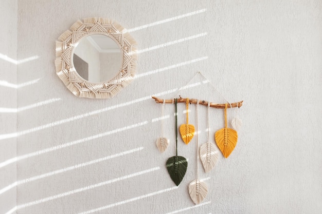Zdjęcie makrama lustro i liście makrama wiszące na ścianie w kolorze żółtym, białym, zielonym i naturalnym kolorze na drewnianym patyku