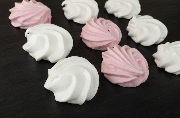 Makro zdjęcie zbliżenie ciasteczka biały i różowy beza. Tradycyjny wzór merengues, pieczony krem do ubijania na czarnym łupku spożywczym, makieta beze płaska lay