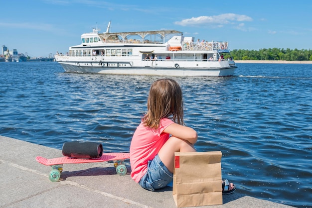 Mała 67-letnia dziewczynka patrzy na łódź i wodę siedzącą na brzegu rzeki Widok z tyłu