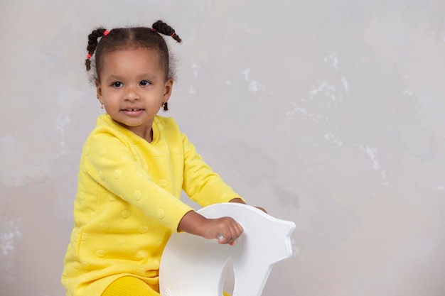 Mała afroamerykańska dziewczynka w żółtych ubraniach pokazuje język Śmieszne dziecko