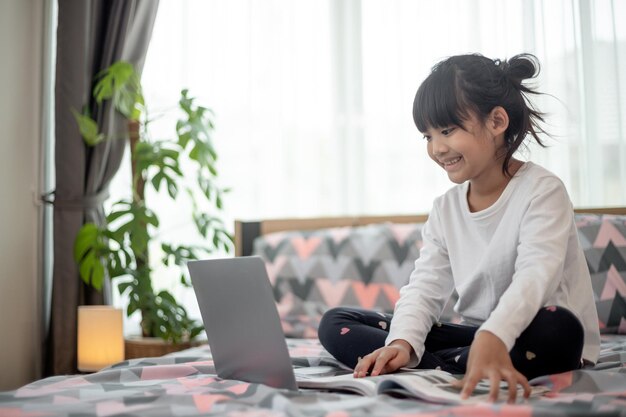 Mała Azjatka korzysta z laptopa leżąc na łóżku