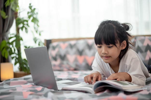 Mała Azjatka korzysta z laptopa leżąc na łóżku