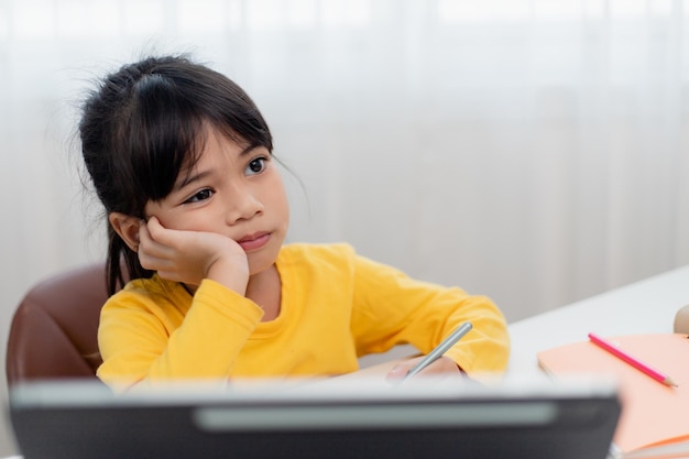 Mała Azjatka siedzi samotnie i patrzy ze znudzoną twarzą Dziecko w wieku przedszkolnym kładzie głowę na stole ze smutnym znudzonym odrabianiem prac domowych rozpieszczone dziecko