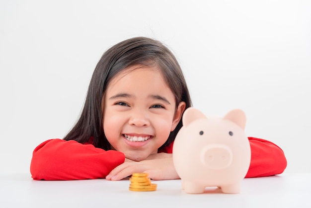 Mała azjatycka dziewczynka oszczędza pieniądze w skarbonce, ucząc się o oszczędzaniu pieniędzy na przyszłą edukację