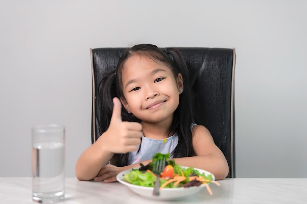 Mała azjatycka urocza dziewczyna do jedzenia zdrowych warzywOdżywianie i zdrowe nawyki żywieniowe dla koncepcji dzieciDzieci szczęśliwe i lubią jeść warzywa