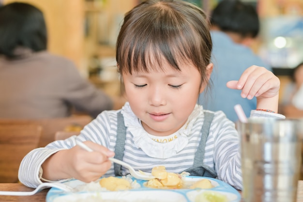 Mała Azjatykcia Dziecko Dziewczyny Use łyżka Czerpać Jedzenie Na Stole Jeść. Podczas Lunchu Na Stole W Restauracji