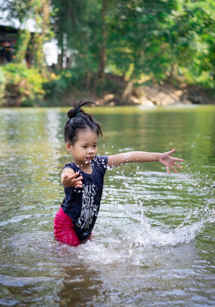 Mała azjatykcia dziewczyna bawić się w rzece z wodnym pluśnięciem
