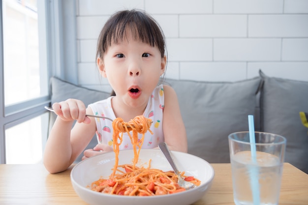 Mała azjatykcia dziewczyna cieszy się łasowanie spaghetti na stole przy restauracją