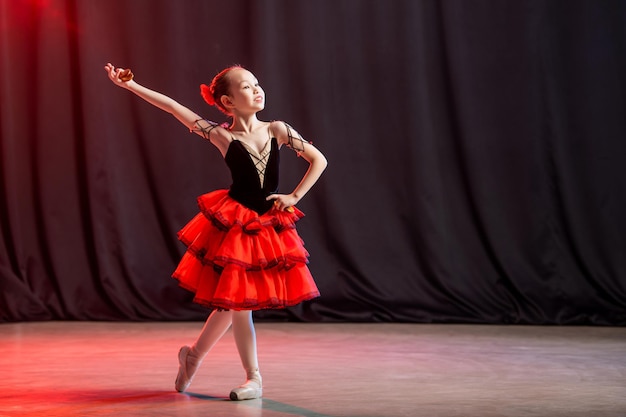 Mała baletnica tańczy na scenie w tutu na pointach z kastaniedami, klasyczną odmianą Kitri.