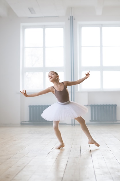 Mała baletnica w sukience tutu wykonująca taniec baletowy sama w sali tanecznej