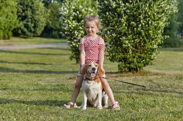 Mała biała dziewczynka bawi się latem na ulicy z psem rasy beagle